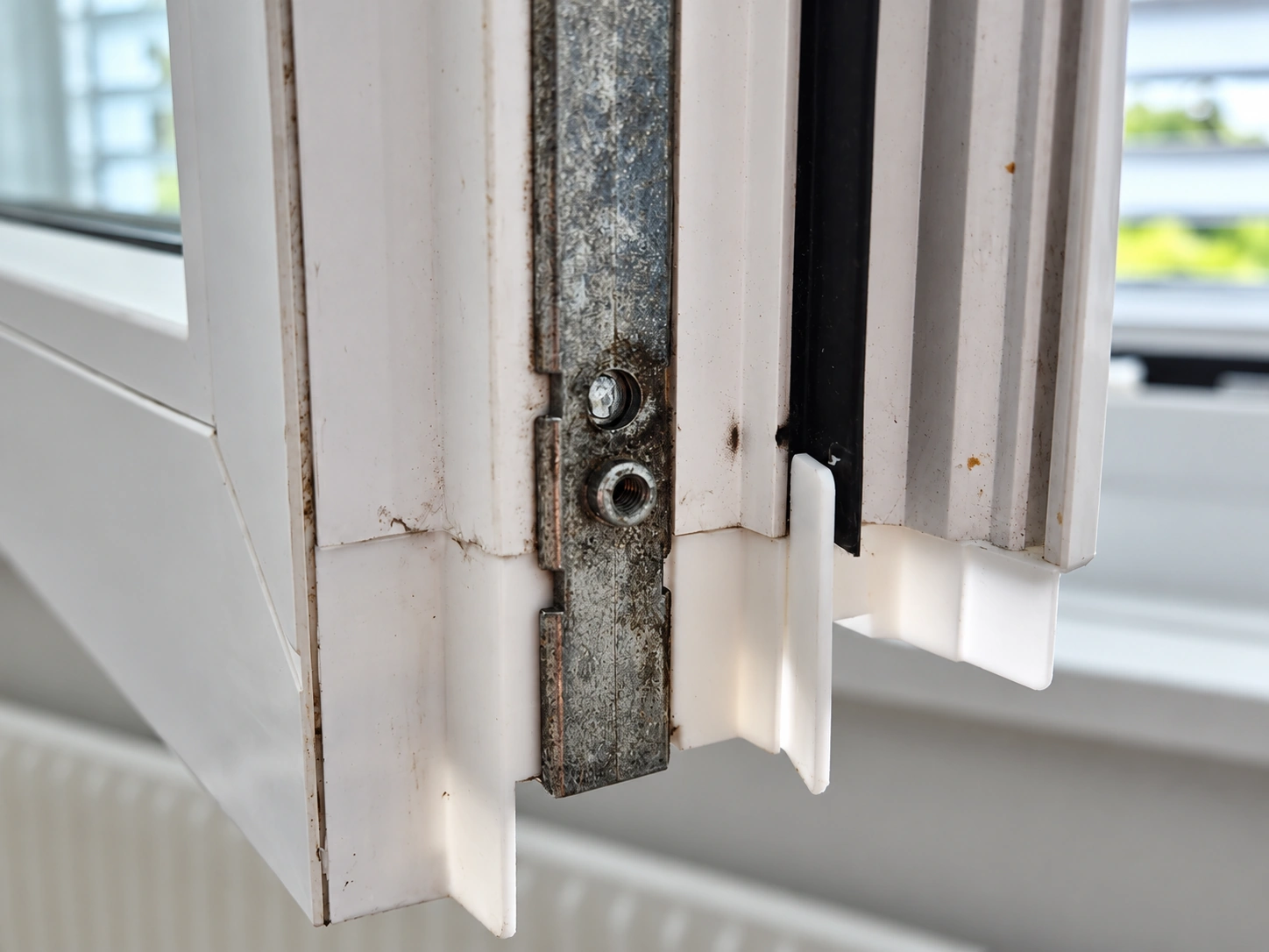 Nahaufnahme eines geöffneten Fensters mit Metallbeschlag und weissem Kunststoffteil