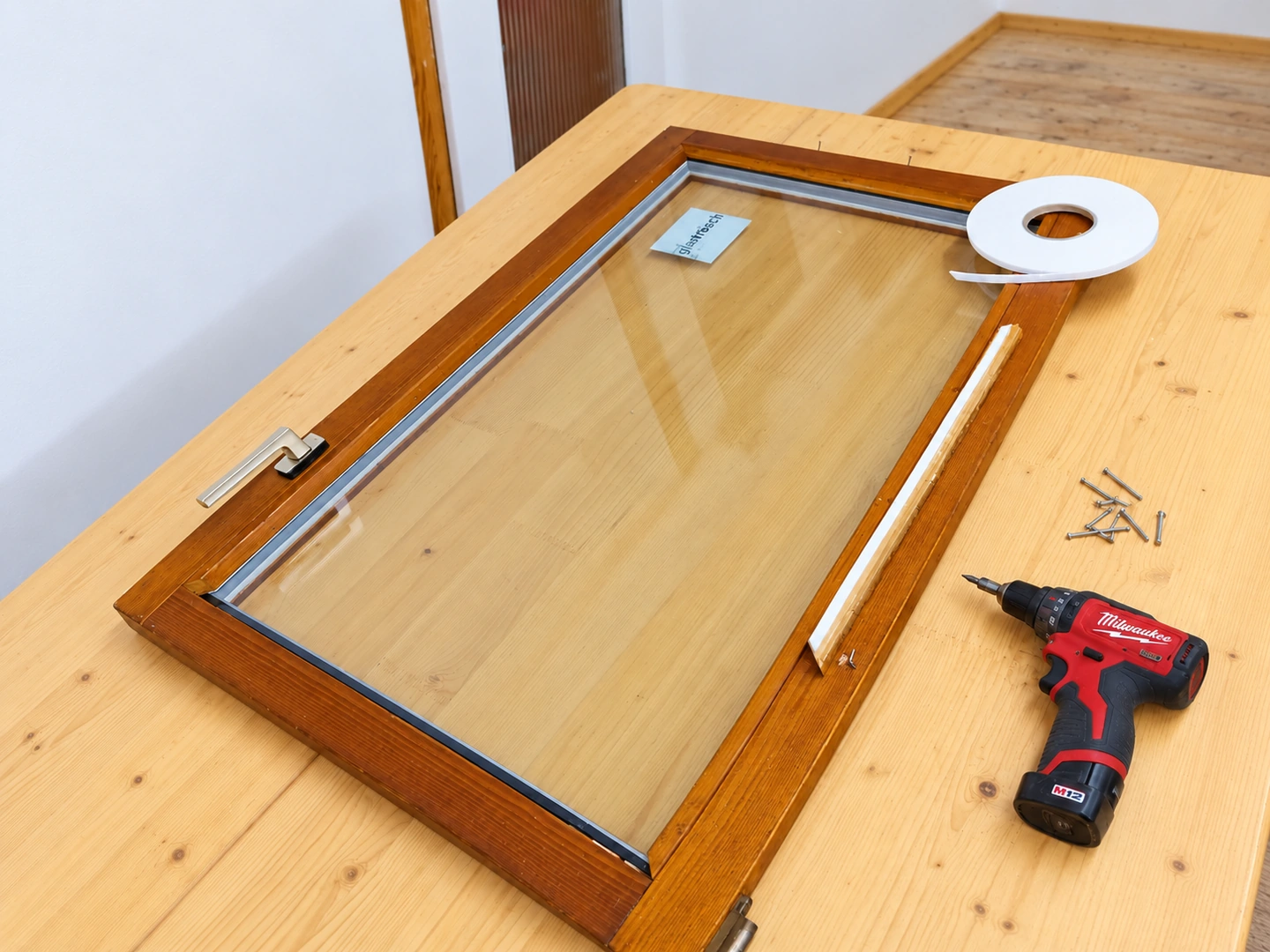Holzfenster bei der Reparatur mit Glaserband, gelöster Glasleiste und bereitgelegtem Werkzeug